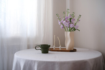 A beautifully serene table display that features delicate flowers in ceramic vase, an elegant green mug, and candles.