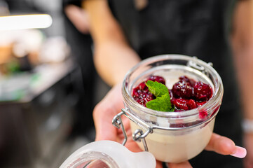 A server presents a charming dessert in a glass jar filled with creamy panna cotta, topped with...