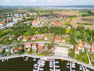 Aerial view of a picturesque lakeside town in Poland featuring vibrant houses, a marina, and lush greenery under a bright sky.