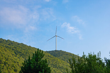 Wind turbine on a forested hill under a clear sky. Single wind power generator in natural forest...