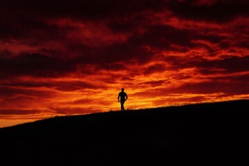 Silhouette of an athlete walking on a hill at sunset with a dramatic red and orange sky in the background