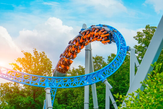 Loop metal frame of a roller coaster in an amusement park. Rollercoaster cart with people riding it goes high speed through loop upside down in trees bushes city park