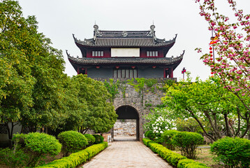 Historic stone gate covered in greenery with traditional architecture in a serene garden setting