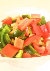 Close-up of freshly chopped red and green bell peppers in a plastic container.