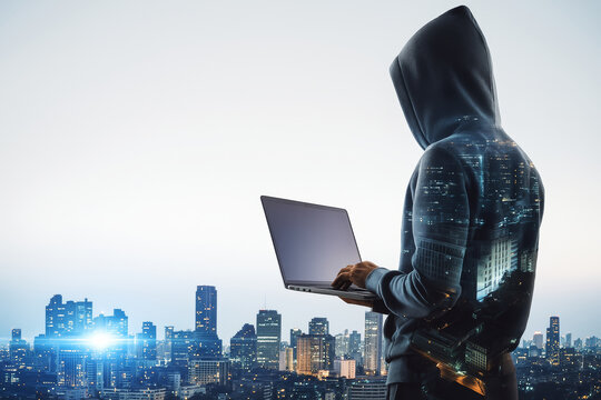 Anonymous hacker in hoodie using laptop on city rooftop with digital overlay of buildings and lights on light background, symbolizing cybercrime concept.