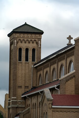 Obraz premium Historic Brick Church with Tower and Cross Against Cloudy Sky