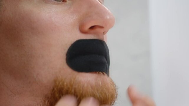 Man Pressing Black Hostage Tape Breathable Mouth Tape onto Lips with Both Hands in Extreme Close-Up for Sleep Aid Concept