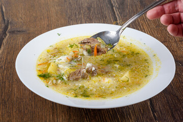 A spoonful of Leningrad rassolnik soup with beef in a rich golden broth.