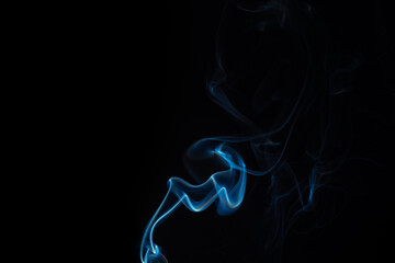 Obraz premium Wispy blue smoke wave flowing against a black background, creating a sense of mystery and elegance. Abstract and atmospheric concept. Swirling, writhing smoke to overlay on your photos