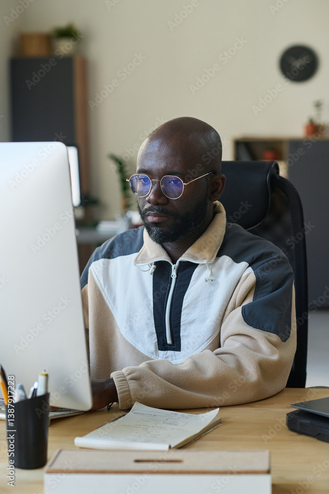 Poster African American male software developer working over new product while sitting in front of computer monitor and looking at screen