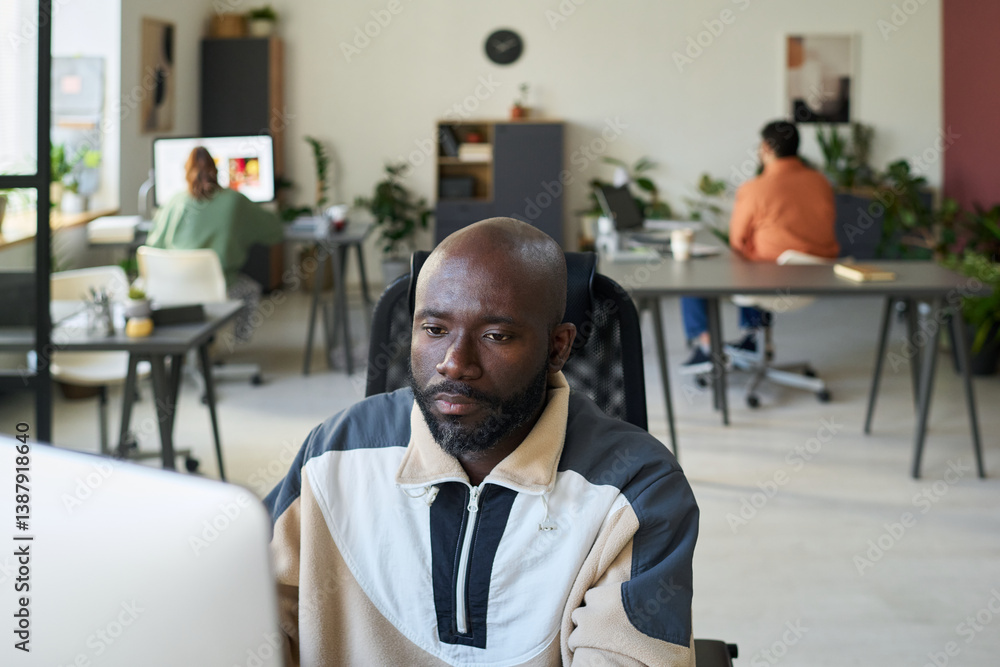 Fototapete young serious african american programmer sitting by workplace in front of desktop computer and look