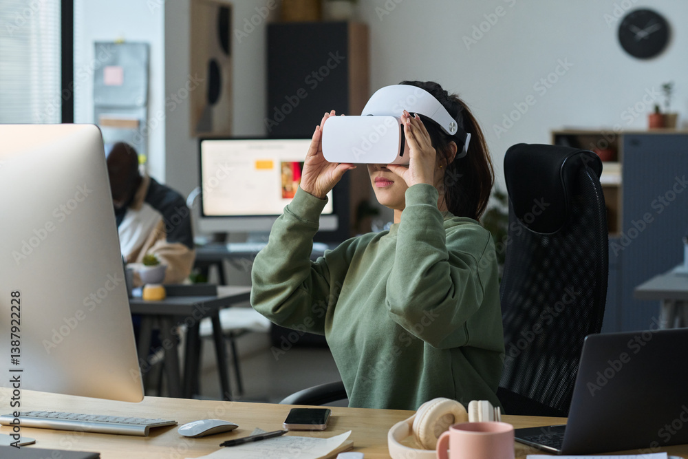 Aufkleber young female designer in vr helmet sitting by workplace in office and looking through virtual slides