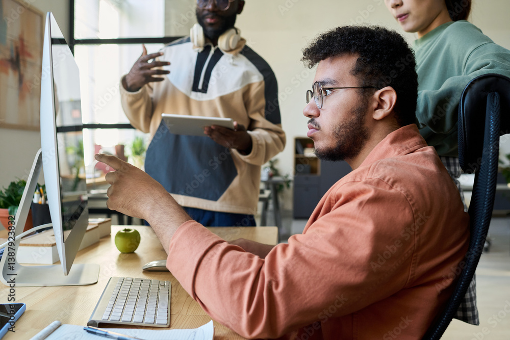 Poster Side view of young multiethnic male programmer pointing at computer screen with code or new software product