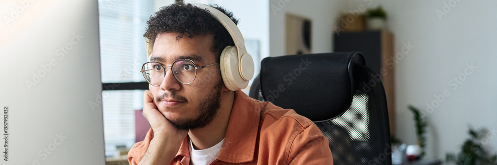 Aufkleber header of young serious man in headphones looking at computer screen while watching online video by 
