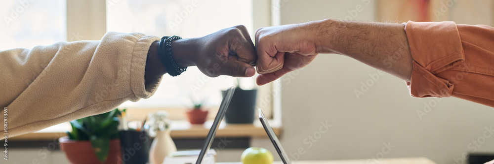 Poster Header of punch bump of two young intercultural male programmers over laptops during work over new software in office