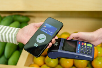 Digital wallet payment approved using smartphone by Asian adult female at fruit shop counter during...