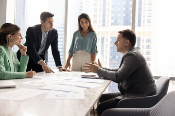 Motivated Caucasian project manager man talking to Latin colleague at team meeting, offering...