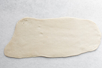 Overhead view of chinese scallion pancake dough being rolled on white countertop, top view of homemade scallion pancakes, process of making cong you bing