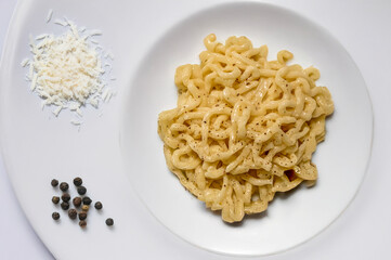Traditional Italian cacio e pepe pasta dish on white ceramic, with grated Pecorino Romano cheese and black peppercorns. Minimalist composition, warm and creamy tones, light background.