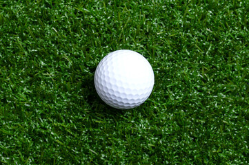 Golf ball on artificial turf, close up. Single, white American golf ball with special notches, on a flat plastic grass surface, with empty space for text or other purposes. Studio shot, from above.