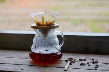 Black coffee in a glass pitcher of a coffee dripper set placed on a wooden counter.