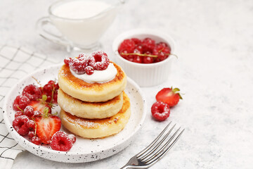 Traditional russian and ukrainian dish for breakfast syrniki. Cottage cheese pancakes with sour cream and fresh berries on white marble background. Side view