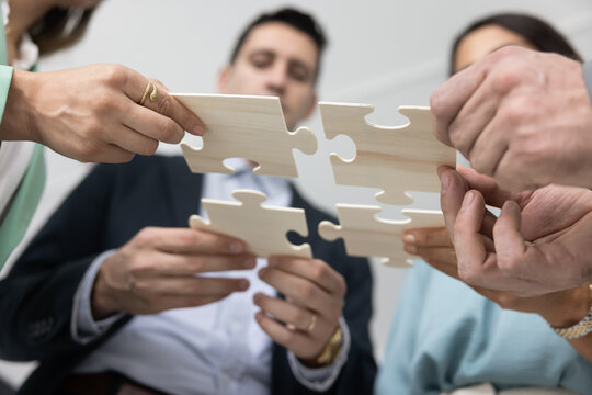 Young business team joining pieces of jigsaw low bottom view. Company colleagues connecting puzzle parts together, symbolizing teamwork, teambuilding, synergy, finding solution