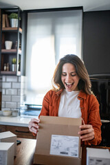 Excited woman opening package at home in kitchen
