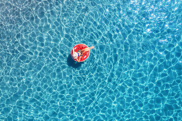 Aerial view of a woman swimming with red swim ring in blue sea at sunrise in summer. Tropical...