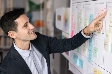Happy confident young Hispanic company director working on tasking, analyzing sticky notes on...