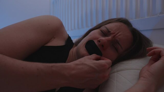 Woman in Bed Frustrated While Removing Breathable Mouth Tape with Eyes Closed in Dim Light Before Falling Asleep Without It for Sleep Discomfort Concept