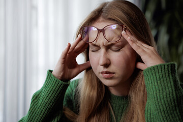 Young woman with headache touching temples, showing signs of stress or fatigue at home or work.