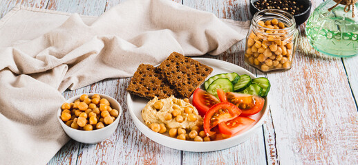 Hummus, chickpeas, tomato, cucumber, grain crackers on a plate on the table web banner
