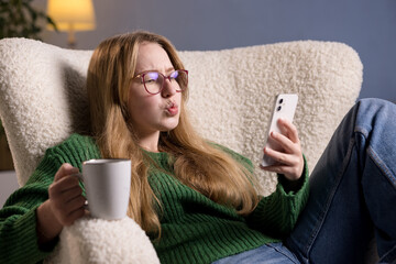 Woman with coffee and smartphone shows surprised expression while reading something online at home.