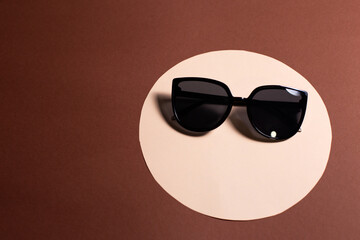 Sunglasses, black glasses on a peach circle, on a brown background