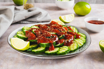Mexican spicy cucumbers with chili sauce and lime on a plate on the table