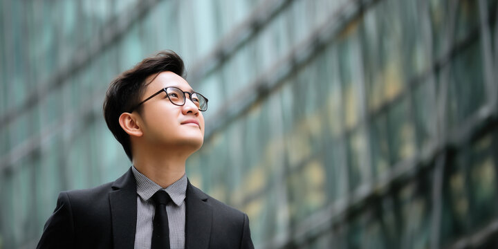 confident young businessman formal attire gazes upward with optimism against modern glass