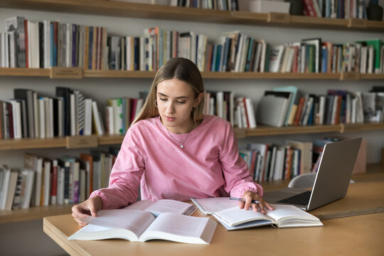 Diligent student at work. Busy gen z woman engaged in remote learning self training session at classroom or library read paper literature use notebook to browse information online take notes by hand
