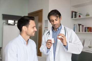 Portuguese man doctor in coat with stethoscope around his neck holding pill bottle and explaining...