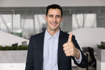 Happy confident handsome young Latin business leader man showing thumb up gesture at camera, making...