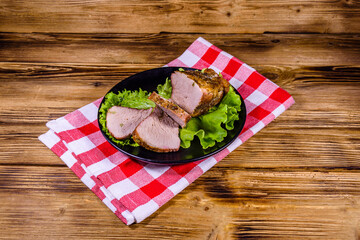 Slices of baked pork meat and lettuce leaves on a black plate