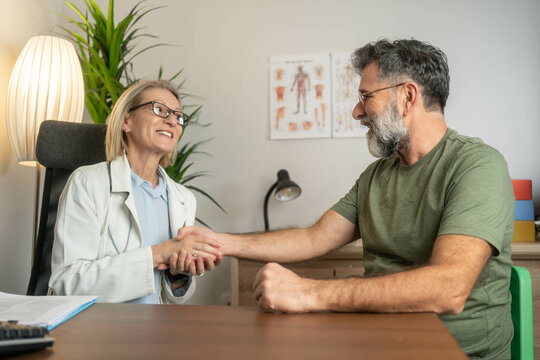 Smiling female doctor shaking hands with male patient in doctor's office. Friendly and professional healthcare provider offering a warm greeting in a clinical setting. Diversity in Healthcare 