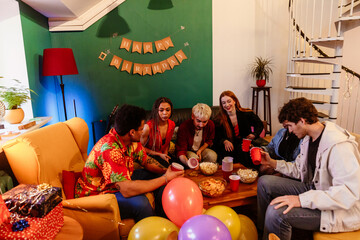 Group of six friends sitting at a table and holding cups while talking and laughing at a party