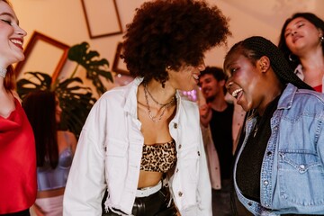 Group of four female friends standing and talking while laughing and looking at each other, at a party