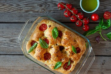 Fresh Italian flat bread Focaccia with tomatoes, olives, garlic and herbs on a wooden background.