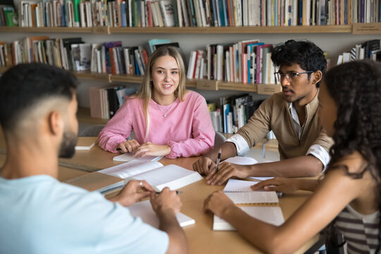 Round table peer learning. Successful group of 4 diverse multicultural students pupils engaged in scientific conversation at campus library study together using paper notes books to discuss assignment