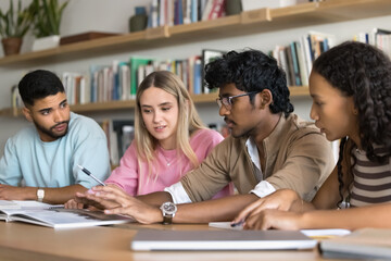 Group study and informal leadership. Smart teenage guy sit at desk in library speak to diverse...