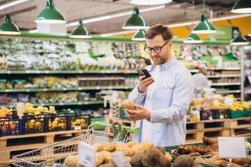 Man using smartphone and choosing potatoes in supermarket