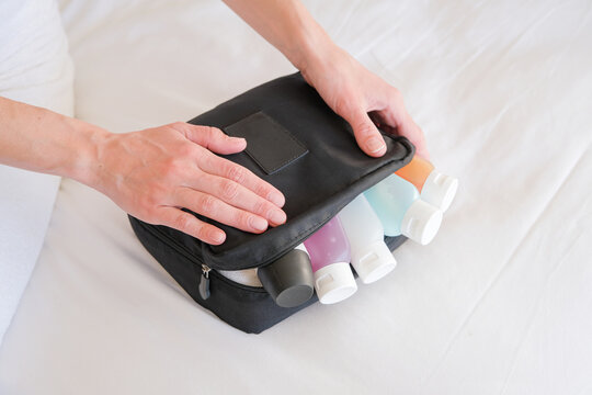 woman hands holding cosmetic travel kit on the bed. colorful cosmetic bottles