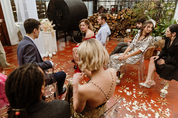 A group of eight guests sit on chairs and talk to each other, before the wedding ceremony